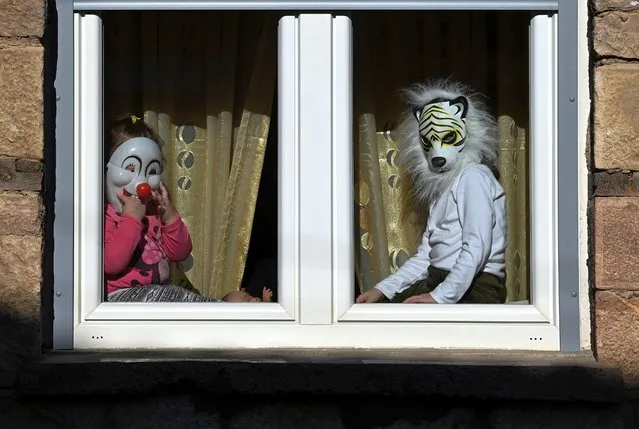 Children wearing masks watch the carnival procession from a window of their house on the first day of a carnival celebration marking the Orthodox St. Vasilij Day in the village of Vevcani, Republic of North Macedonia, 13 January 2022. The Vevcani Carnival is one of the most famous village festivals in the Balkans. It is believed that the custom is over 1,400 years old and based on pagan beliefs. Essentially the carnival is the ritual of calling after Saint Basil the Great, which coincides with the Twelve Days of the Orthodox Christmas and the Orthodox New Year. The festivity is held on 13 and 14 January every year. People in Vevcanci believe that with their masks they banish evil spirits from their lives. The participants of the carnival are known as Vasilicari. The highlights of the carnival include a political satire where masked villagers act out current events. In 1993, the carnival and the village of Vevcani officially became a part of the World Federation of Carnival Cities. (Photo by Georgi Licovski/EPA/EFE)