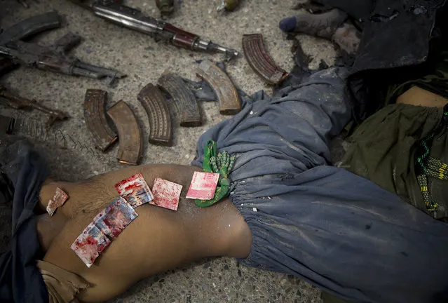 In this Wednesday, March 12, 2014 file photo made by Associated Press photographer Anja Niedringhaus, Pakistani bank notes covered in blood are displayed on the body of a dead suicide bomber after police found them in his pocket after an attack on the former Afghan intelligence headquarters, in the center of Kandahar, Afghanistan. (Photo by Anja Niedringhaus/AP Photo)