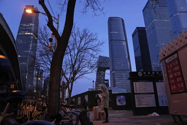 A resident looks at her phone near skyscrapers at the central business district in Beijing, China, Wednesday, January 26, 2022. Richer, more heavily armed and openly confrontational, China has undergone history-making change since the last time it was an Olympic host in 2008. (Photo by Ng Han Guan/AP Photo)