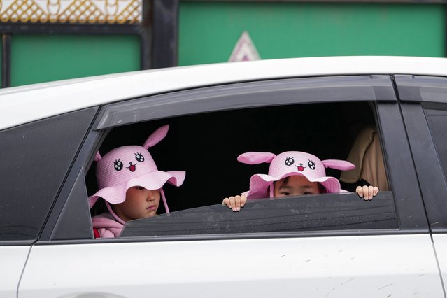 Children wearing hats with cartoon faces wait in a car outside a polling station in a ger district on the outskirts of Ulaanbaatar, Mongolia, Friday, June 28, 2024. Voters in Mongolia are electing a new parliament on Friday in their landlocked democracy that is squeezed between China and Russia, two much larger authoritarian states. (Photo by Ng Han Guan/AP Photo)