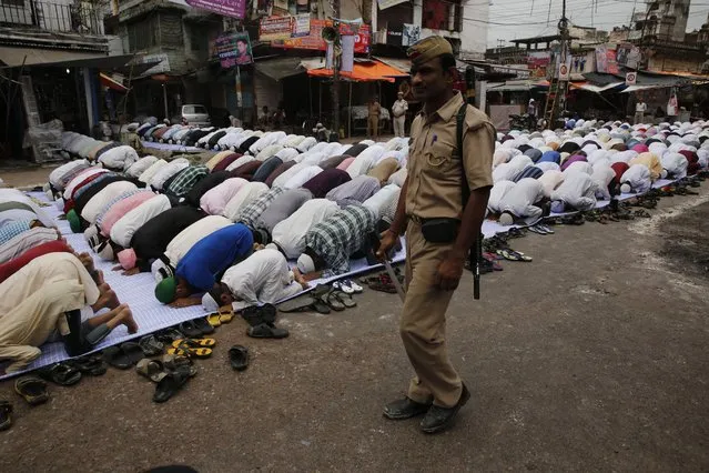 An Indian policeman walks as Muslims pray on a road outside the Jama Masjid on the last Friday of Ramadan in Allahabad, India, Friday, July 17, 2015. The day Eid ul-Fitr is celebrated depends on the sighting of the new moon and confusion often prevails when the Imams in one part of India spot the moon and others don't. It's not unusual for the festival to be celebrated on different days in different parts of India. (Photo by Rajesh Kumar Singh/AP Photo)