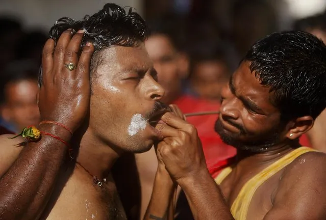 An Indian Hindu devotee reacts in pain as he gets his cheeks pierced with a steel rod as part of a ritual during an annual pilgrimage to the temple of Hindu goddess Sheetla Mata in Jammu, India, Sunday, July 26, 2015. (Photo by Channi Anand/AP Photo)