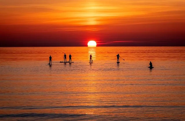 Paddle boarders tour the calm Baltic Sea in Timmendorfer Strand northern Germany as the sun rises on a cold Monday, morning, April 18, 2022. (Photo by Michael Probst/AP Photo)