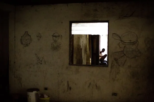 In this June 26, 2015 photo, single mother Manushka Doneis, 18, sits inside the abandoned shipping company building where she lives with her siblings and five-month-old daughter in Port-au-Prince, Haiti. Haitians who are homeless since the 2010 earthquake can be found living in the best conditions they can find – the ruins of a luxury hotel, makeshift shelters on the grounds of the destroyed national theater, and even in one case in an unventilated trailer. (Photo by Rebecca Blackwell/AP Photo)