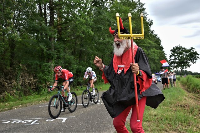 Didi Senft, a cycling enthusiast better known as “El Diablo” (The Devil) cheers along the roadside as AG2R Citroen Team's French rider Benoit Cosnefroy (C) and Team Arkea - Samsic's French rider Anthony Delaplace (L) cycle in a breakaway during the 4th stage of the 110th edition of the Tour de France cycling race, 182 km between Dax and Nogaro, in southwestern France, on July 4, 2023. (Photo by Marco Bertorello/AFP Photo)