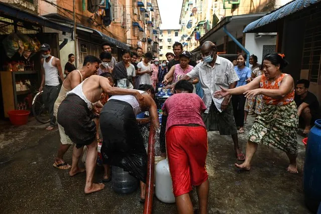 People react as water sprays while filling up containers in Yangon on March 14, 2022, as thousands of people faced water shortages due to power outages in the city. (Photo by AFP Photo/Stringer)