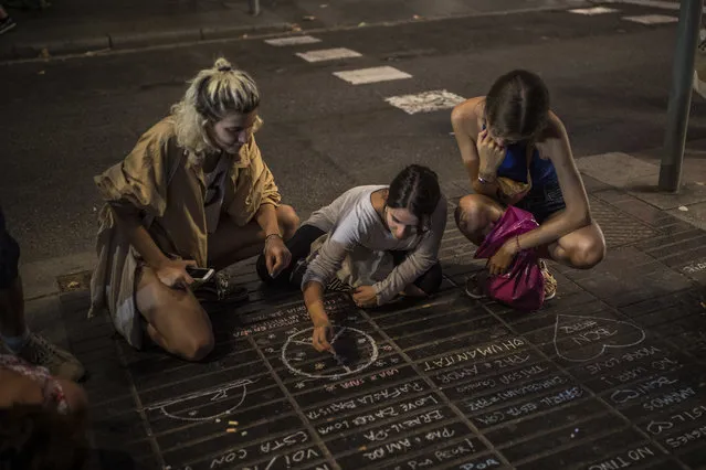 A girl draws a peace symbol on the street as a tribute to the victims of the terrorist attack, on the historic street of Las Ramblas, two day after the vehicle attacks, in Barcelona, Spain, Friday August 18, 2017. Authorities in Spain and France pressed the search Saturday for the supposed ringleader of an Islamic extremist cell that carried out vehicle attacks in Barcelona and a seaside resort, as the investigation focused on links among the Moroccan members and the house where they plotted the carnage. (Photo by Santi Palacios/AP Photo)