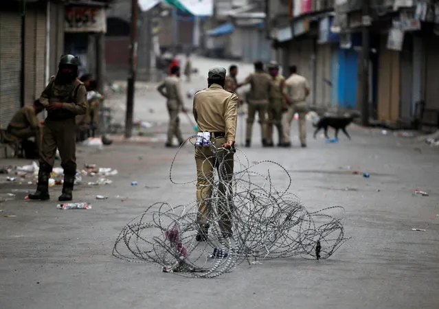 An Indian policeman pulls concertina wire to lay a barricade on a road during a curfew in Srinagar July 12, 2016. (Photo by Danish Ismail/Reuters)