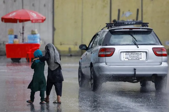 Two Afghan children walk under the rain on a street in Kabul, Afghanistan on August 2, 2022. (Photo by Ali Khara/Reuters)