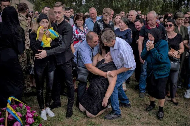 Olga Gregorievna Styglyuk, 55, faints next to a coffin with the body of her soon Yury Styglyuk, a Ukrainian serviceman who died in combat on August 24 in Maryinka, Donetsk, during his funeral in Bucha, Ukraine, Wednesday, August 31, 2022. (Photo by Emilio Morenatti/AP Photo)