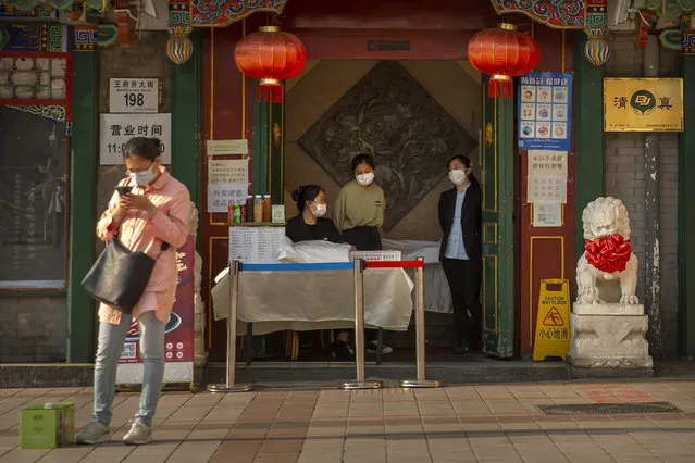Clerks wear face masks to prevent the spread of the new coronavirus as they wait for customers at the entrance to a restaurant in Beijing, Tuesday, April 28, 2020. (Photo by Mark Schiefelbein/AP Photo)