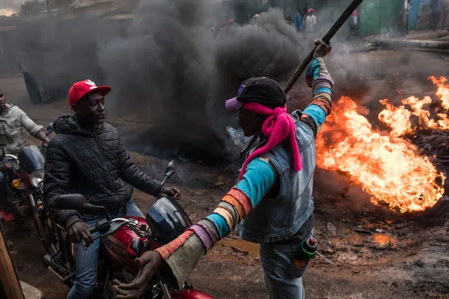 A man stops motorcycles in front of a burning roadblock lit in protest for opposition presidential candidate Raila Odinga, in the Kibera slum, on October 25, 2017 in Nairobi, Kenya. (Photo by Andrew Renneisen/Getty Images)