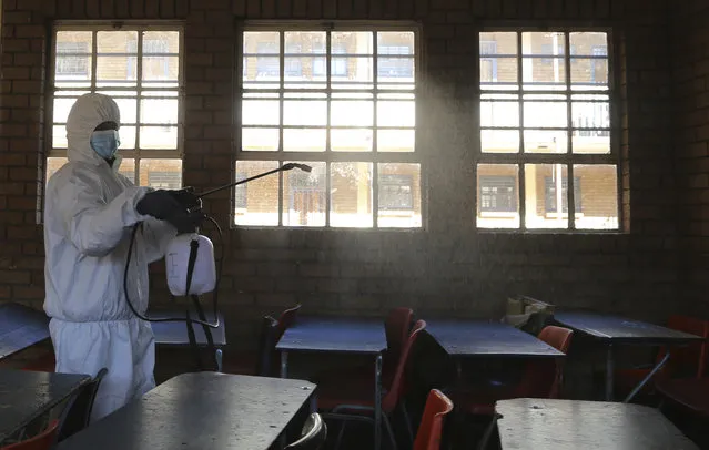 A worker from Bidvest Prestige wearing protective gear, sprays disinfectant in a classroom to help reduce the spread the new coronavirus ahead of the reopening of Landulwazi Comprehensive School, east of Johannesburg, South Africa, Tuesday, May 26, 2020, ahead of the June 1, 2020, re-opening of Grade 7 and 12 learners to school. (Photo by Themba Hadebe/AP Photo)