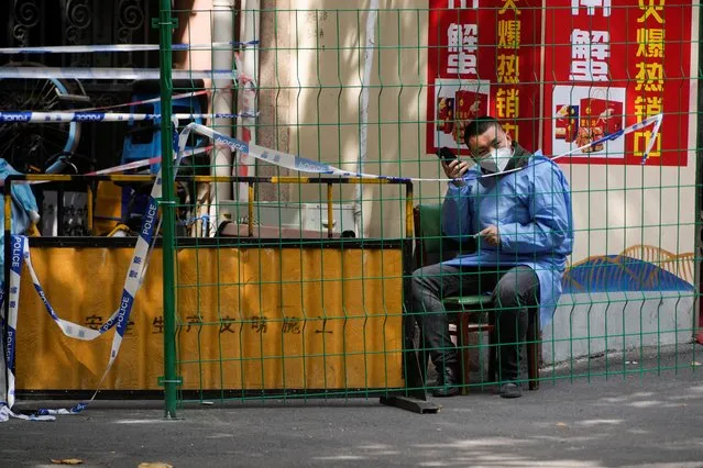 A worker in a protective suit talks on a phone behind a barrier at a sealed area following the coronavirus outbreak, in Shanghai, China on October 11, 2022. Shanghai and other big Chinese cities, including Shenzhen, have ramped up testing for COVID-19 as infections rise, with some local authorities hastily closing schools, entertainment venues and tourist spots. (Photo by Aly Song/Reuters)