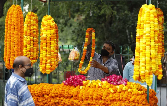 A roadside flower vendor covers his face with a mask and sells flowers outside a temple, in Prayagraj, India, Monday, June 8, 2020. Religious places, malls, hotels and restaurants open Monday after more than two months of lockdown as a precaution against coronavirus. (Photo by Rajesh Kumar Singh/AP Photo)