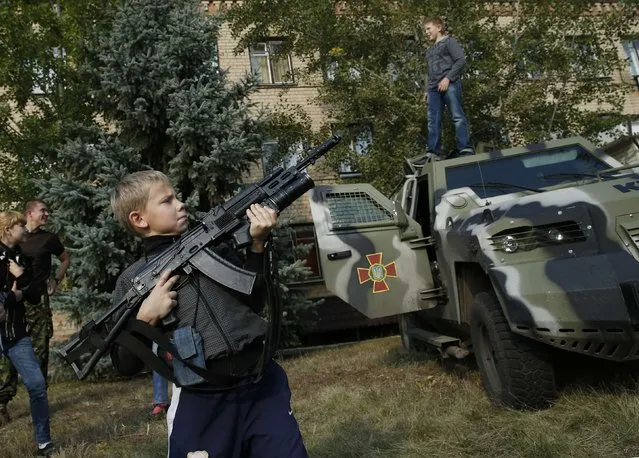 A boy holds up a secured Kalashnikov assault rifle while interacting with Ukrainian solders in Soledar, eastern Ukraine September 27, 2014. The children were supervised by the soldiers while handling weapons. (Photo by David Mdzinarishvili/Reuters)