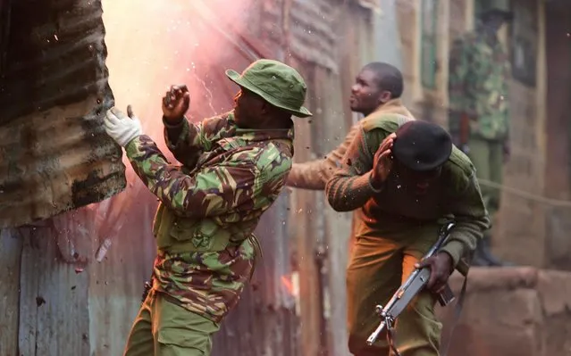 Police try to extinguish a fire lit by opposition supporters after four people were killed in the Mathare area in Nairobi, Kenya, Sunday, November 19, 2017. Kenyan opposition leaders say police are using gunfire and tear gas to disperse residents of a city slum protesting the overnight murder of four people in a suspected ethnic attack. (Photo by Brian Inganga/AP Photo)