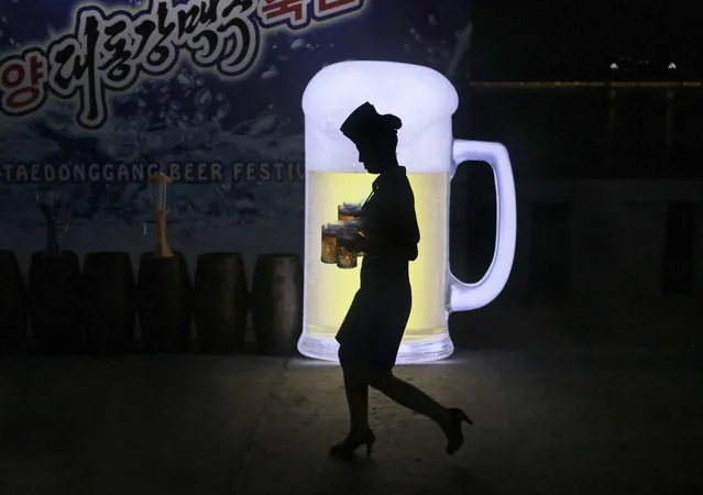 A waitress is silhouetted against an advertisement board as she carries jugs of beer during Taedonggang Beer Festival in Pyongyang, North Korea, Sunday, August 21, 2016. The festival, the first of its kind in the country, was held as a promotional event for the locally brewed beer. (Photo by Dita Alangkara/AP Photo)