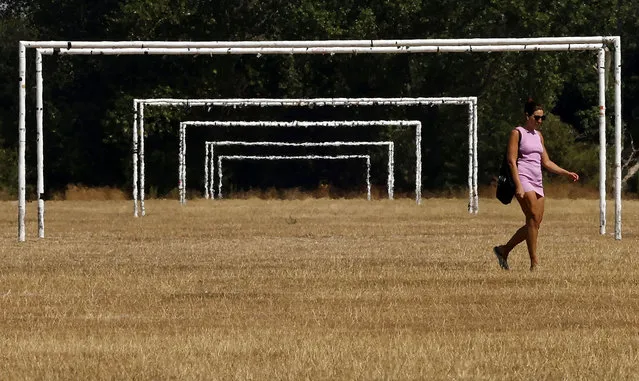 A woman walks in the heat past the goalposts on the scorched, dry grass on Hackney Marshes in London on August 13, 2022. The UK government on Friday officially declared a drought across swathes of England, following months of record low rainfall and unprecedented high temperatures in recent weeks. (Photo by Carlos Jasso/AFP Photo)