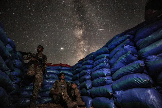 This long-exposure picture taken early on July 23, 2020, shows the Milky Way galaxy rising in the sky above Syrian fighters of the Turkish-backed National Front for Liberation group while on watch duty between sandbags in the town of Taftanaz along the frontlines in the country's rebel-held northwestern Idlib province. (Photo by Omar Haj Kadour/AFP Photo)