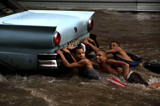 Youths hang from the rear bumper of a vintage American car as they play in a flooded street, after a heavy rain in Havana, Cuba, Wednesday, October 14, 2015. (Photo by Ramon Espinosa/AP Photo)