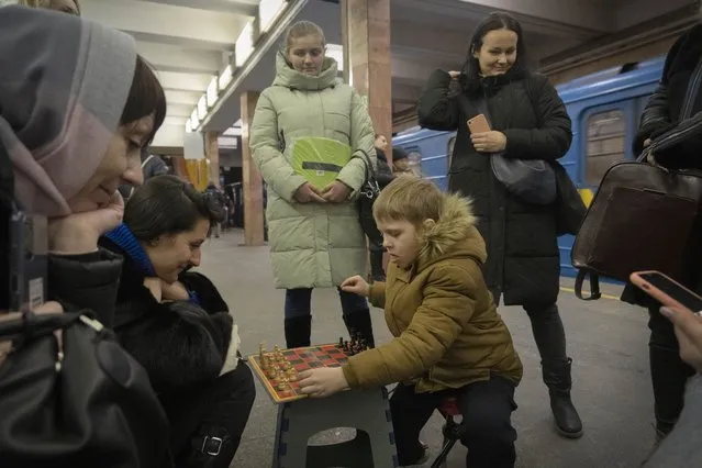 A boy and a woman play chess as other people watch in a subway station being used as a bomb shelter during a Russian rocket attack in Kyiv, Ukraine, Friday, February 10, 2023. (Photo by Efrem Lukatsky/AP Photo)