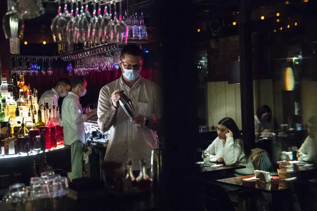 A bartender wearing face mask to protect against coronavirus makes a cocktail at Strelka bar in Moscow, Russia, Friday, October 23, 2020. In much of Europe, city squares and streets, be they wide, elegant boulevards like in Paris or cobblestoned alleys in Rome, serve as animated evening extensions of drawing rooms and living rooms. As Coronavirus restrictions once again put limitations on how we live and socialize, AP photographers across Europe delivered a snapshot of how Friday evening, the gateway to the weekend, looks and feels. (Photo by Pavel Golovkin/AP Photo)