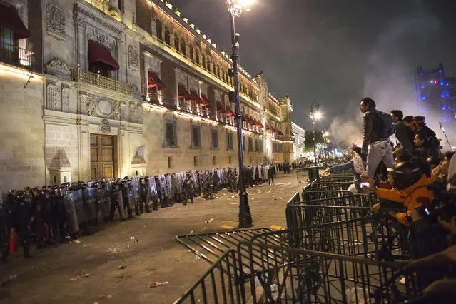 In this November 20, 2014 file photo, protestors face off against federal police over barriers surrounding the National Palace in Mexico City. Protesters marched in the capital city to demand authorities find 43 missing college students, seeking to pressure the government. Mexico officially lists more than 20,000 people as having gone missing since the start of the country's drug war in 2006, and the search for the missing students has turned up other, unrelated mass graves. (Photo by Rebecca Blackwell/AP Photo)