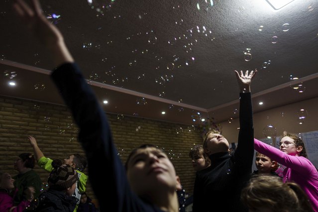 Children reach out for soap balloons during celebrations of St. Nicholas Day in Izium, Ukraine, December 6, 2024. (Photo by Evgeniy Maloletka/AP Photo)