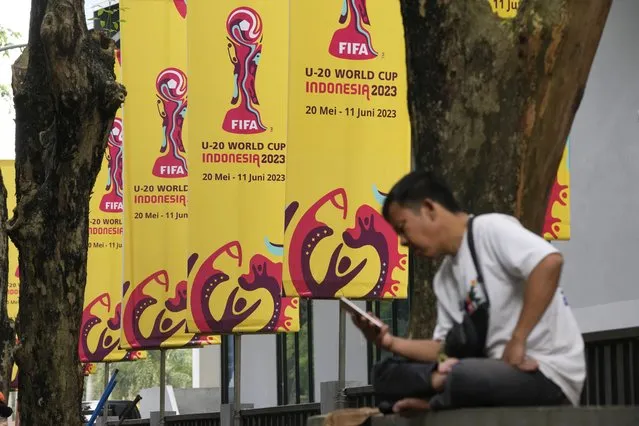 A man checks his mobile phone near banners of FIFA U-20 World Cup in Jakarta, Indonesia, Thursday, March 30, 2023. Indonesia was stripped of hosting rights for the Under-20 World Cup on Wednesday only eight weeks before the start of the tournament amid political turmoil regarding Israel's participation. (Photo by Dita Alangkara/AP Photo)