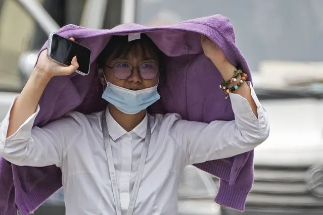 A woman uses a sweater to shield from the sun as she walls on a street on a hot day in Beijing, Monday, July 3, 2023. (Photo by Andy Wong/AP Photo)