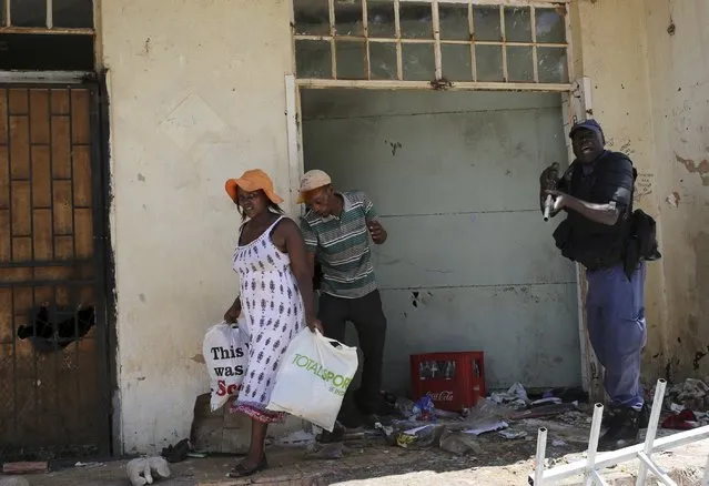 A policeman (R) reacts as locals loot from a shop, believed to be owned by a foreigner, during service delivery protests in Mohlakeng, west of Johannesburg February 4, 2015. (Photo by Siphiwe Sibeko/Reuters)
