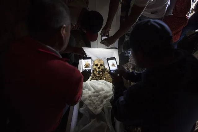In this August 14, 2018 photo, relatives take cell phone pictures of the remains of Fortunate Ventura Huamacusi, a man who was killed by the Peruvian army in 1983, before placing the coffin in its niche at the Rosaspata cemetery in Peru's Ayacucho province. Thousands of Peruvian families who have spent decades wondering about loved ones who disappeared during years of bloody conflict between the state and Maoist guerrillas have new hopes for getting the closure they have been searching for. (Photo by Rodrigo Abd/AP Photo)
