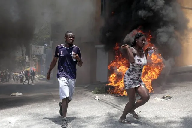 Demonstrators run past tires set on fire during a protest against insecurity in Port-au-Prince, Haiti, Monday, August 7, 2023. (Photo by Joseph Odelyn/AP Photo)