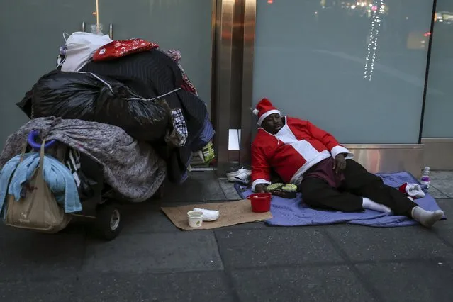 A homeless man dressed as Santa Claus sleeps on the ground during unseasonably warm weather on Christmas eve in the Manhattan borough of New York December 24, 2015. (Photo by Carlo Allegri/Reuters)