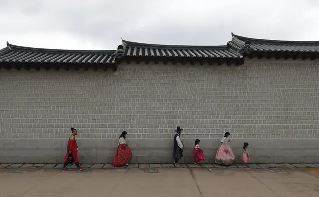 Visitors dressed in South Korean traditional “Hanbok” attire walk along a wall in a line protecting themselves from a rain outside the Gyeongbok Palace, the main royal palace during the Joseon Dynasty, and one of South Korea's well known landmarks in Seoul, South Korea, Thursday, July 12, 2018. (Photo by Lee Jin-man/AP Photo)