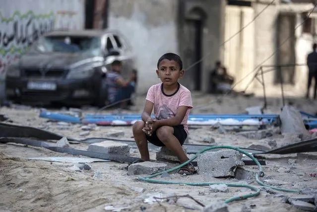 A Palestinian boy sits looking at others inspecting the damage of their shops following Israeli airstrikes on Jabaliya refugee camp, northern Gaza Strip, Thursday, May 20, 2021. Heavy airstrikes pummeled a street in the Jabaliya refugee camp in northern Gaza, destroying ramshackle homes with corrugated metal roofs nearby. The military said it struck two underground launchers in the camp used to fire rockets at Tel Aviv. (Photo by Khalil Hamra/AP Photo)