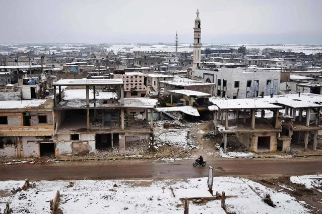 A Syrian man rides his motorbike past damaged buildings covered with snow on December 18, 2016, in a rebel-held district of Homs. (Photo by Mahmoud Taha/AFP Photo)