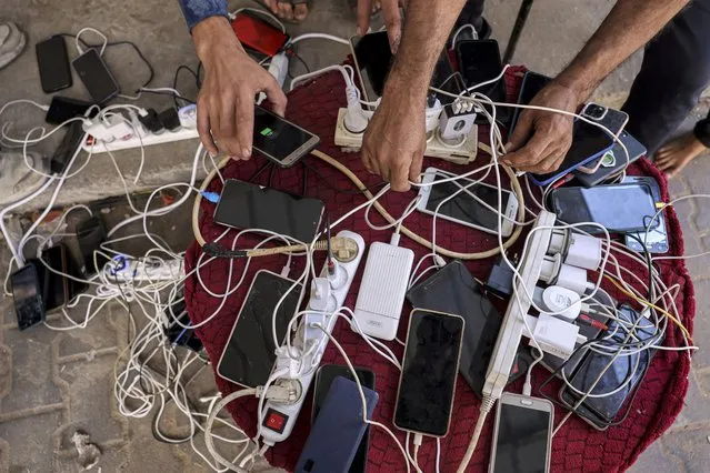 People sit by phone chargers connected to a communal group of electric socket hubs outside a closed pharmacy in Rafah in the southern Gaza Strip on October 20, 2023 amid ongoing battles between Israel and the Palestinian Hamas movement. (Photo by Mohammed Abed/AFP Photo)