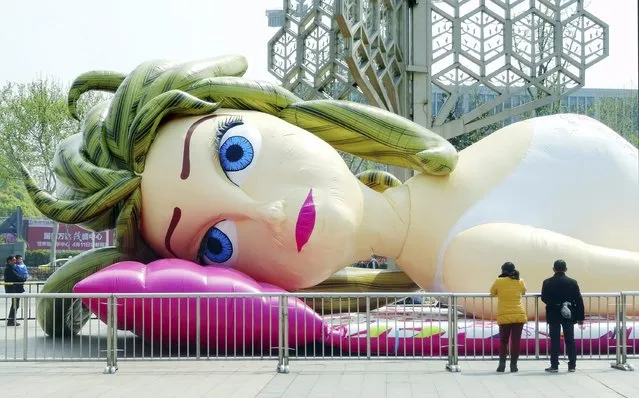 People look at a giant inflated doll in the shape of a woman, on a square in Nanjing, Jiangsu province April 9, 2015. The 30-metre-long, 7-metre-wide doll was made by a local company, and also serves as a inflated “castle” for children to play inside, local media reported. (Photo by Reuters/Stringer)
