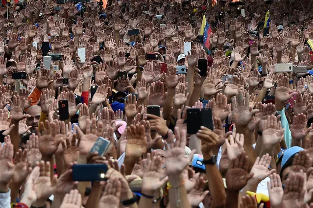 People raise their hands during a mass opposition rally against President Nicolas Maduro in which Venezuela's National Assembly head Juan Guaido (out of frame) declared himself the country's “acting president”, on the anniversary of a 1958 uprising that overthrew a military dictatorship, in Caracas on January 23, 2019. “I swear to formally assume the national executive powers as acting president of Venezuela to end the usurpation, (install) a transitional government and hold free elections”, said Guaido as thousands of supporters cheered. Moments earlier, the loyalist-dominated Supreme Court ordered a criminal investigation of the opposition-controlled legislature. (Photo by Federico Parra/AFP Photo)
