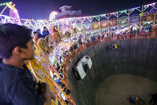 People watch performers at the so-called “Well of Death” show in an amusement park during the annual Mahim Fair in Mumbai, India, 30 December 2023. The ten-day fair features giant wheels, toy trains and gravity-defying stunts in the “Maut Ka Kuan” or 'Well of Death' in honor of the Sufi saint Makhdoom Ali Mahimi. (Photo by Divyakant Solanki/EPA)
