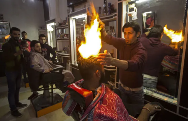 Ramadan Edwan, a Palestinian barber, uses fire in a hair-straightening technique with a client at his salon in the Rafah refugee camp, in the southern Gaza Strip on February 1, 2017. (Photo by Mahmud Hams/AFP Photo)