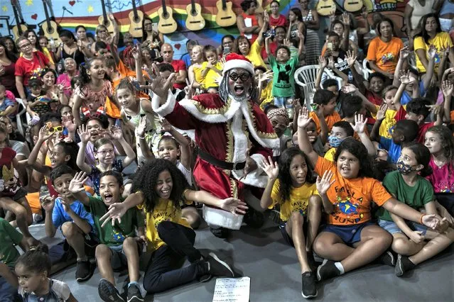 Children pose for photos with Black Santa, played by dance teacher Felipe Canela, at a Christmas event put on by the Favela World organization which develops youth educational activities, in the Caju favela complex of Rio de Janeiro, Brazil, Monday, December 12, 2022. Favela World presents Black Santa to children in the city's favelas as a Christmas character that better reflects their cultural reality. (Photo by Bruna Prado/AP Photo)