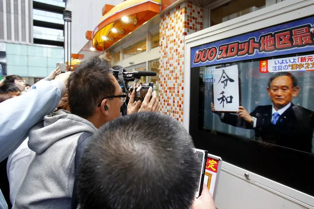 People look at a TV screen showing Japan’s Chief Cabinet Secretary Yoshihide Suga unveiled the name of new era “Reiwa” in a news program in Tokyo, Monday, April 1, 2019. Japan says next emperor Naruhito’s era name is Reiwa, effective May 1 when he takes the throne from his father. (Photo by Koji Sasahara/AP Photo)