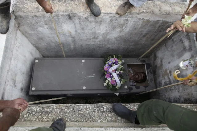 In this February 5, 2014 photo, Divaldo Aguiar, who plays the part of Pachencho, is lowered inside a grave site as he lies inside a mock coffin as part of the Burial of Pachencho celebration at a cemetery in Santiago de Las Vegas, Cuba. (Photo by Franklin Reyes/AP Photo)