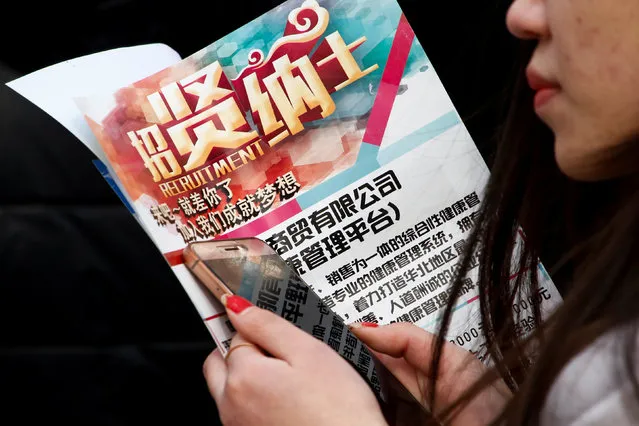A woman holds a company recruitment flyer at a job fair for college graduates and the general public in the centre of Shijiazhuang, Hebei province, China, February 6, 2017. (Photo by Thomas Peter/Reuters)