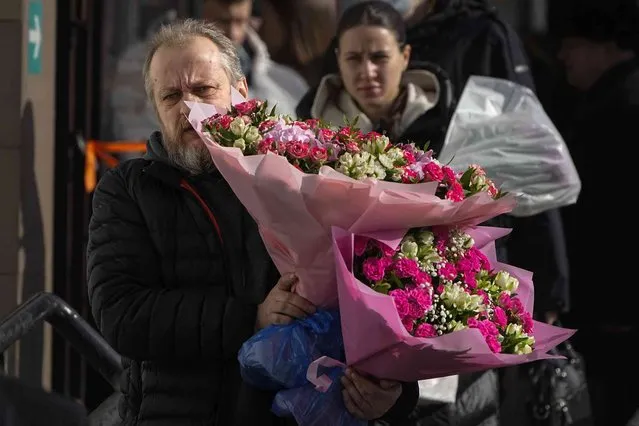 A man carries bunches of flowers purchased from the flower market on International Women's Day, in Moscow, Russia, on Thursday, March 7, 2024. International Women's Day on March 8 is an official holiday in Russia. Per tradition, men give flowers and gifts to female relatives, friends and colleagues, even though in the past two years flowers have become more expensive. (Photo by Alexander Zemlianichenko/AP Photo)