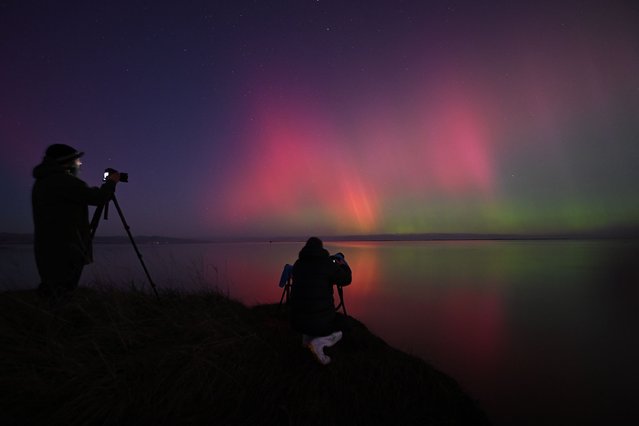 Photographers take pictures of the Aurora Australis, also known as the Southern Lights, glow on the horizon over waters of Lake Ellesmere on the outskirts of Christchurch on May 11, 2024. (Photo by Sanka Vidanagama/AFP Photo)