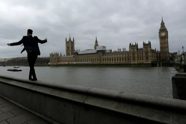 A man balances as he walks along a wall above the River Thames backdropped by the Houses of Parliament and Elizabeth Tower containing the bell know as “Big Ben” in London, Monday, March 20, 2017. Britain's government will begin the process of leaving the European Union on March 29, starting the clock on the two years in which to complete the most important negotiation for a generation. (Photo by Matt Dunham/AP Photo)